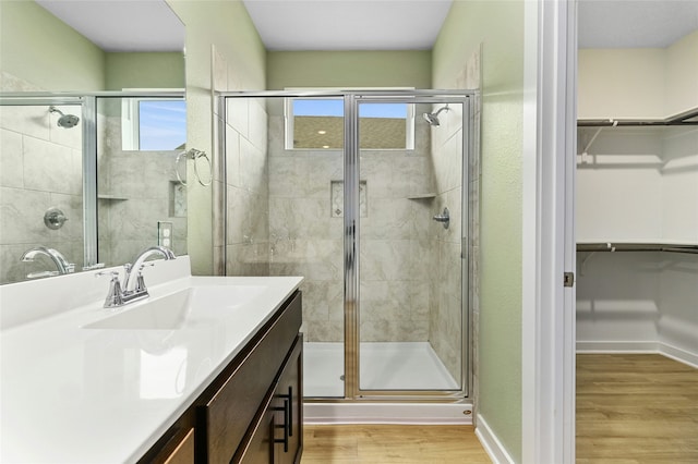 bathroom featuring a stall shower, baseboards, wood finished floors, a spacious closet, and vanity