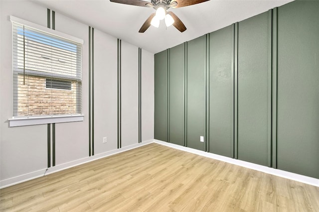 spare room featuring a decorative wall, light wood finished floors, a wealth of natural light, and ceiling fan