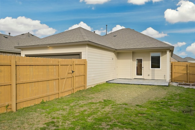 rear view of property featuring roof with shingles, a yard, a patio, an attached garage, and a fenced backyard