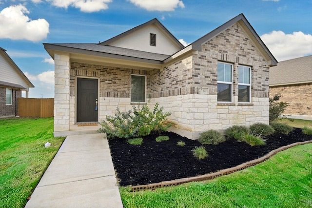 view of front of home featuring a front lawn, fence, stone siding, and a shingled roof