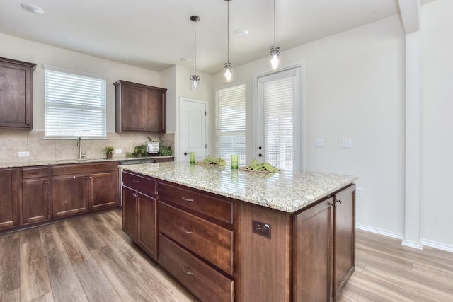 kitchen with hardwood / wood-style floors, a kitchen island, sink, hanging light fixtures, and light stone countertops