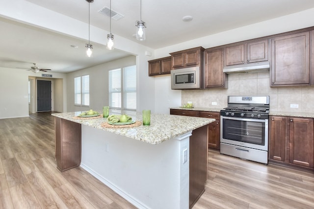 kitchen featuring decorative light fixtures, ceiling fan, light wood-type flooring, appliances with stainless steel finishes, and light stone countertops