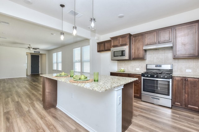 kitchen with ceiling fan, a center island, pendant lighting, stainless steel appliances, and light stone counters