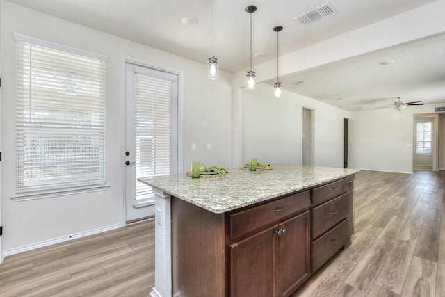 kitchen featuring light stone countertops, pendant lighting, a center island, ceiling fan, and light hardwood / wood-style flooring