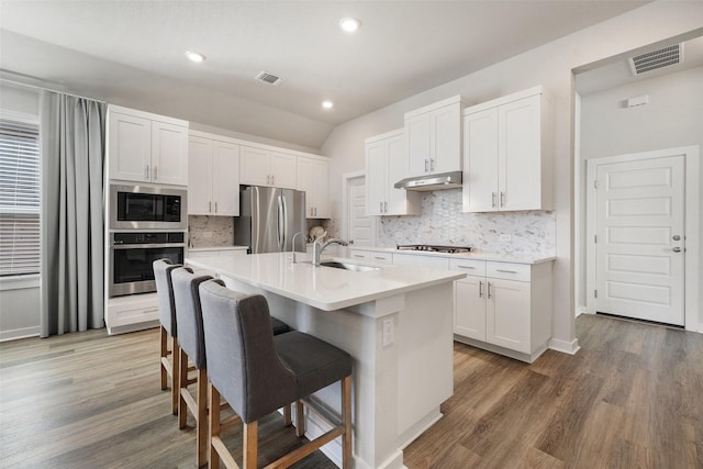 kitchen with white cabinets, stainless steel appliances, an island with sink, sink, and a kitchen breakfast bar