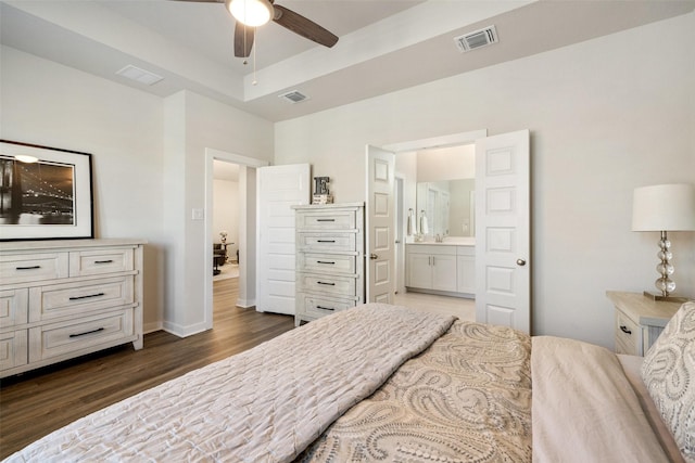 bedroom featuring ensuite bath, ceiling fan, dark wood-type flooring, and a tray ceiling