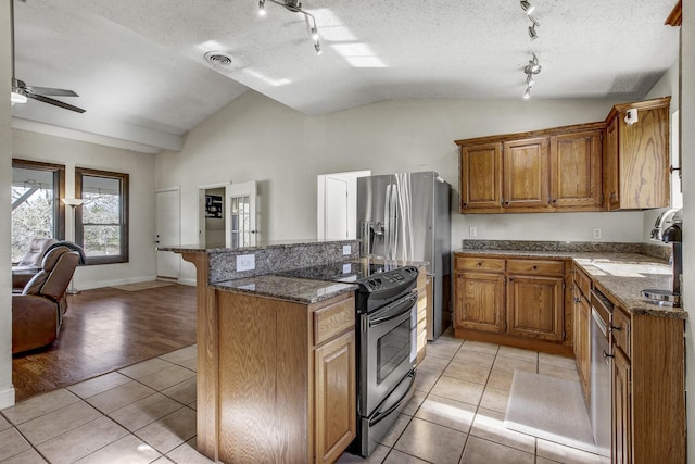 kitchen with a textured ceiling, light tile patterned floors, stainless steel appliances, and lofted ceiling