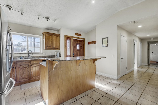 kitchen featuring stone counters, a kitchen island, a breakfast bar, light tile patterned floors, and stainless steel fridge