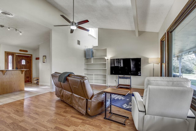 living room featuring ceiling fan, lofted ceiling with beams, light wood-type flooring, and a textured ceiling