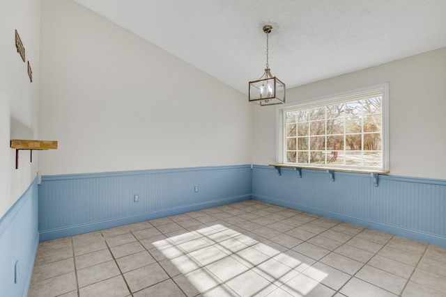 unfurnished room with lofted ceiling, light tile patterned floors, and a notable chandelier