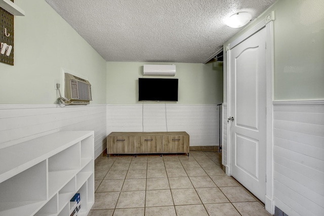 interior space with a textured ceiling, a wall mounted AC, and light tile patterned flooring