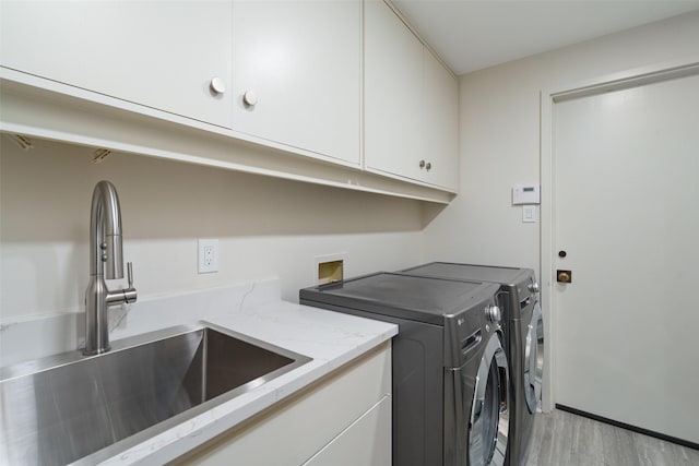 laundry area with cabinets, washer and clothes dryer, light hardwood / wood-style floors, and sink