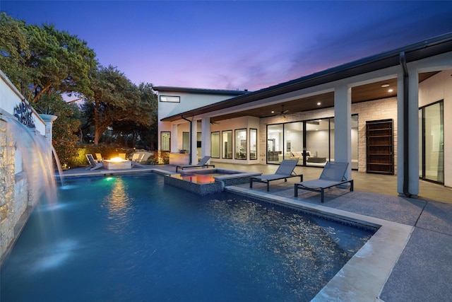 pool at dusk with a fire pit, an in ground hot tub, ceiling fan, and a patio area