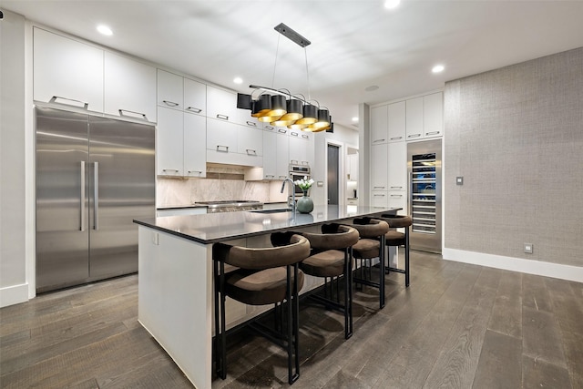 kitchen with a kitchen bar, appliances with stainless steel finishes, white cabinetry, hanging light fixtures, and a kitchen island with sink