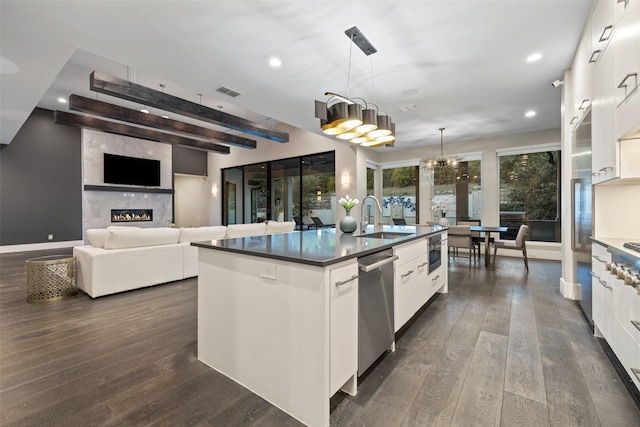 kitchen featuring an island with sink, sink, dishwasher, white cabinets, and hanging light fixtures