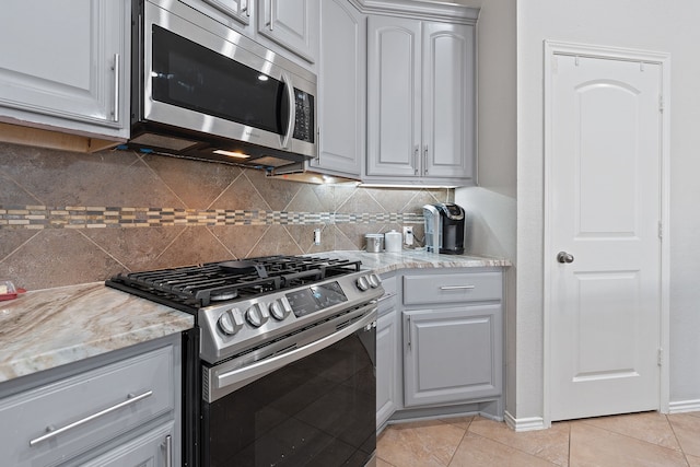 kitchen featuring light tile patterned floors, appliances with stainless steel finishes, gray cabinetry, and light stone counters