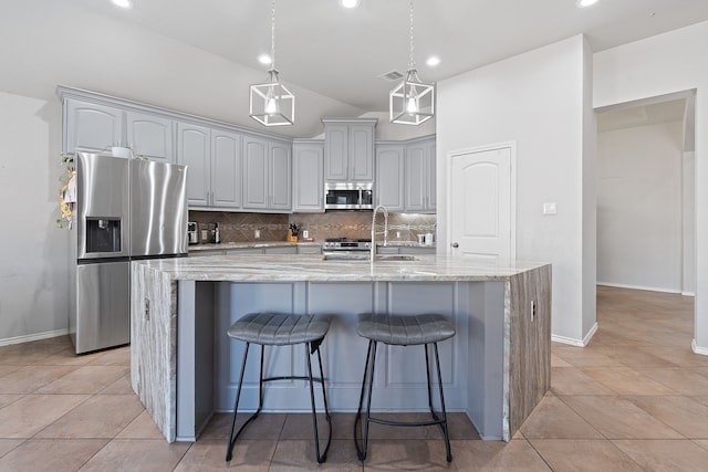 kitchen featuring gray cabinets, sink, light stone countertops, appliances with stainless steel finishes, and an island with sink