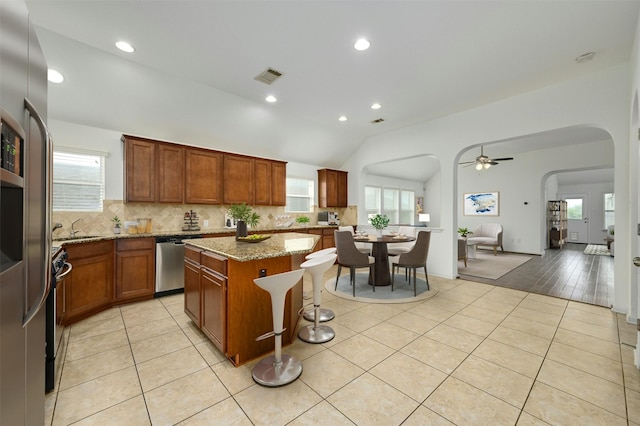 kitchen featuring a center island, light tile patterned floors, ceiling fan, stainless steel appliances, and light stone countertops