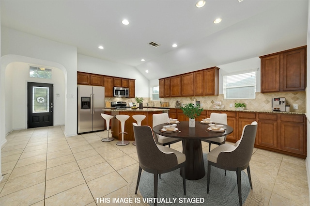 kitchen featuring stainless steel appliances, lofted ceiling, a center island, and light stone counters