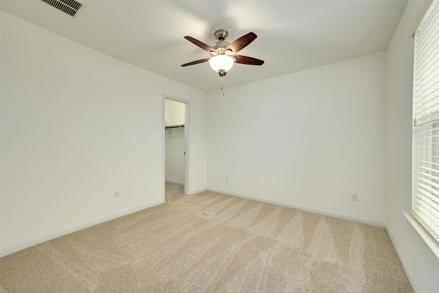 unfurnished bedroom with ceiling fan, a spacious closet, light colored carpet, and multiple windows