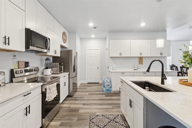 kitchen featuring pendant lighting, sink, white cabinets, light hardwood / wood-style floors, and stainless steel appliances