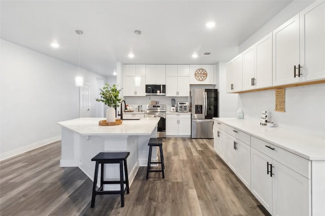 111 Lavender Cv, Dale, TX 78616 - kitchen with stainless steel appliances, recessed lighting, wood finished floors, a breakfast bar area, and white cabinetry
