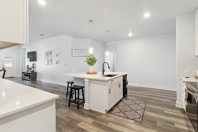 kitchen featuring dark hardwood / wood-style flooring, sink, white cabinets, stainless steel range with electric cooktop, and an island with sink