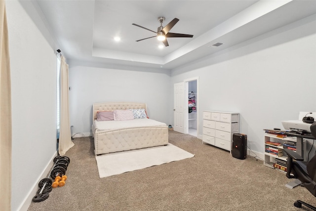 carpeted bedroom with ceiling fan, a raised ceiling, and a spacious closet