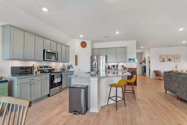 kitchen with tasteful backsplash, a kitchen bar, a kitchen island with sink, appliances with stainless steel finishes, and light stone counters