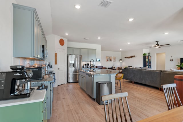 kitchen featuring light hardwood / wood-style floors, a center island with sink, decorative backsplash, sink, and stainless steel appliances