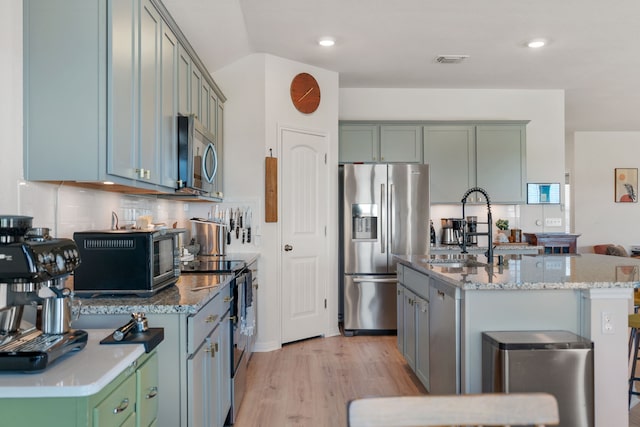 kitchen with sink, an island with sink, appliances with stainless steel finishes, and tasteful backsplash