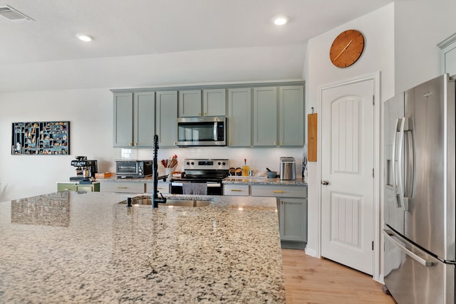 kitchen featuring lofted ceiling, decorative backsplash, light wood-type flooring, light stone countertops, and appliances with stainless steel finishes