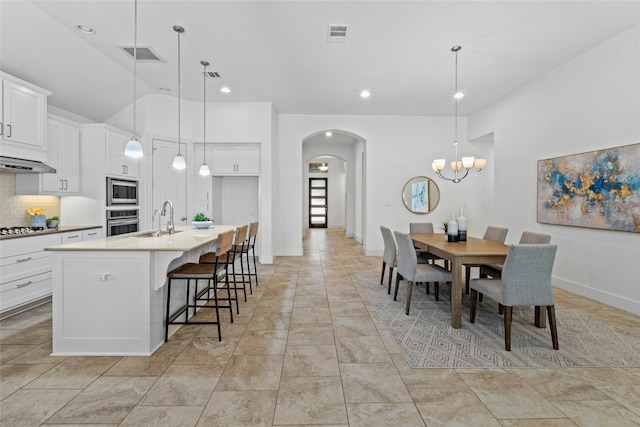 kitchen featuring white cabinets, appliances with stainless steel finishes, sink, hanging light fixtures, and a center island with sink