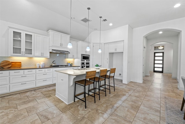 kitchen with white cabinets, exhaust hood, decorative light fixtures, stainless steel appliances, and a kitchen island with sink