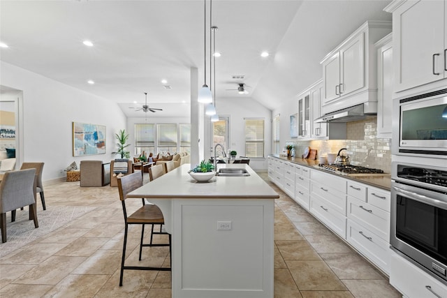 kitchen featuring white cabinetry, stainless steel appliances, sink, vaulted ceiling, and a center island with sink