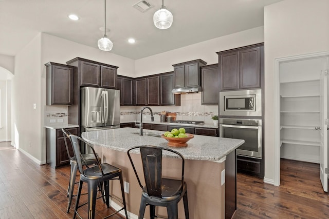 kitchen featuring sink, light stone counters, decorative light fixtures, appliances with stainless steel finishes, and an island with sink