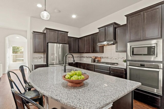 kitchen with light stone counters, appliances with stainless steel finishes, sink, and a center island with sink