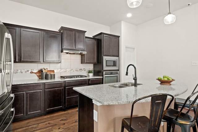 kitchen featuring appliances with stainless steel finishes, a sink, dark wood-type flooring, a breakfast bar, and light stone countertops