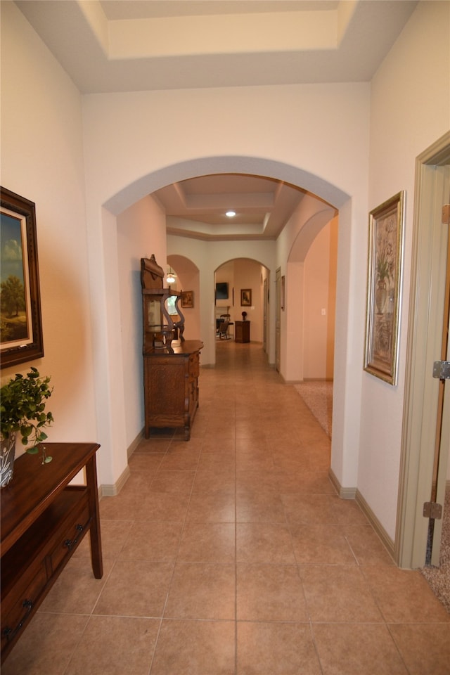 corridor featuring a raised ceiling and light tile patterned flooring