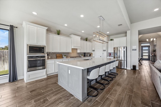 kitchen with appliances with stainless steel finishes, white cabinetry, an island with sink, a notable chandelier, and a breakfast bar