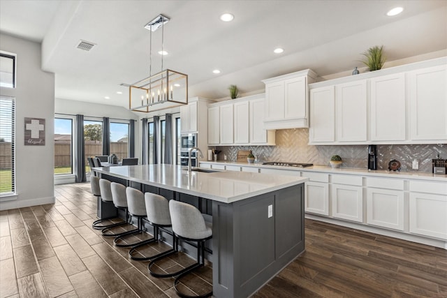 kitchen with white cabinets, hanging light fixtures, and an island with sink