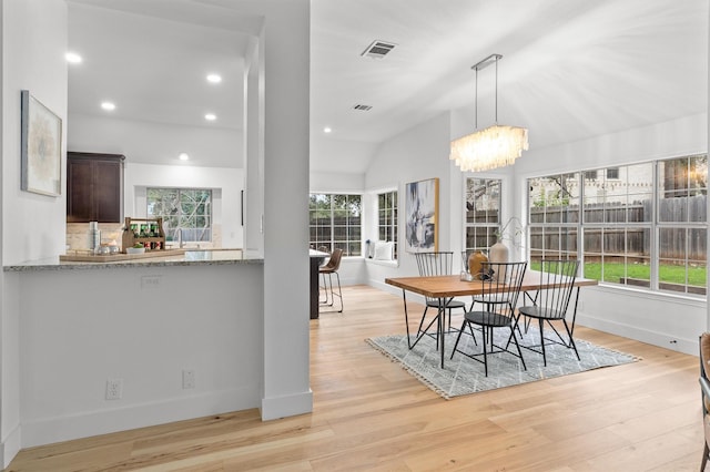 dining room with a wealth of natural light, light hardwood / wood-style flooring, lofted ceiling, and a notable chandelier