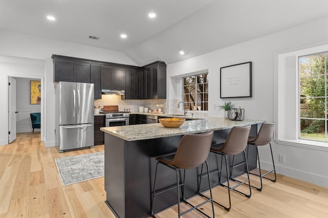 kitchen with vaulted ceiling, appliances with stainless steel finishes, kitchen peninsula, and a kitchen breakfast bar