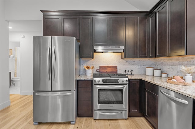 kitchen with dark brown cabinetry, stainless steel appliances, tasteful backsplash, light stone counters, and light hardwood / wood-style flooring