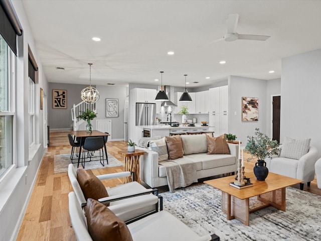 living room with ceiling fan with notable chandelier and light hardwood / wood-style flooring