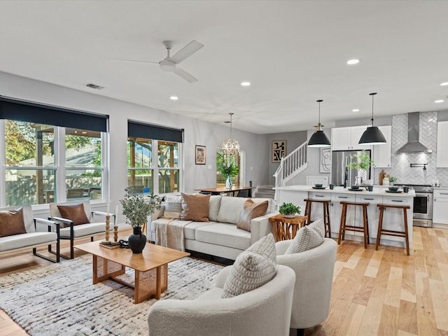 living room with ceiling fan with notable chandelier and light hardwood / wood-style flooring