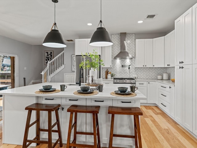 kitchen featuring white cabinetry, a center island, wall chimney exhaust hood, and stainless steel appliances