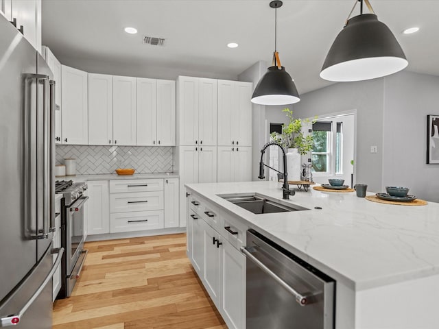 kitchen with pendant lighting, white cabinetry, sink, light stone counters, and high quality appliances