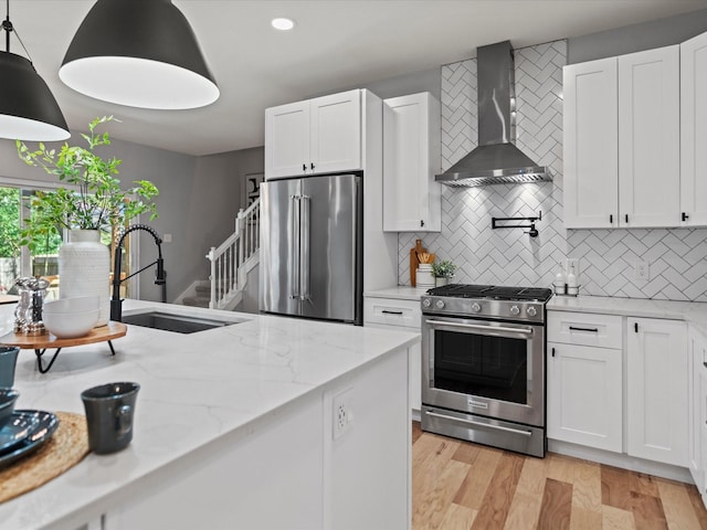 kitchen featuring stainless steel appliances, decorative light fixtures, wall chimney range hood, white cabinets, and sink