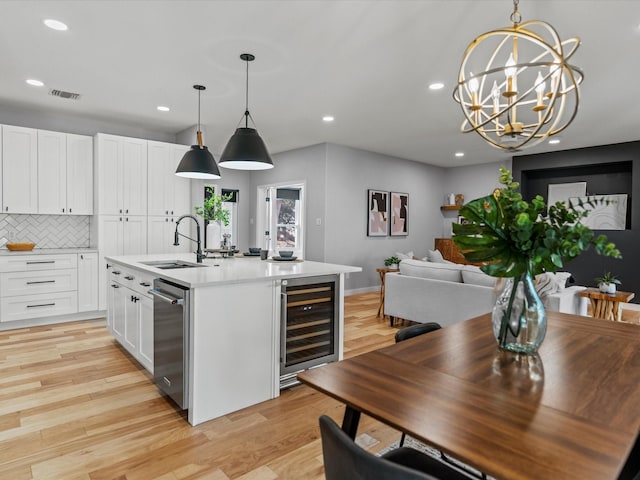 kitchen featuring wine cooler, a center island with sink, sink, hanging light fixtures, and white cabinets